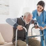 Doctor helping to retired man, getting up from sofa