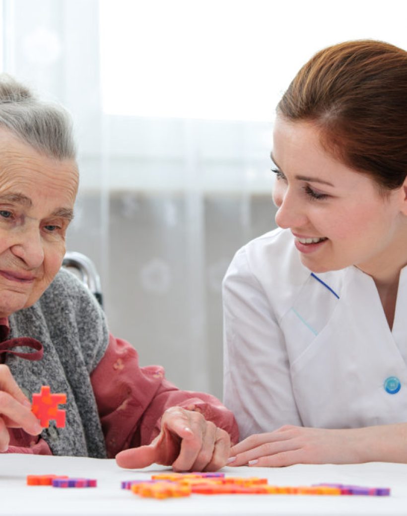 Elder care nurse playing jigsaw puzzle with senior woman in nursing home